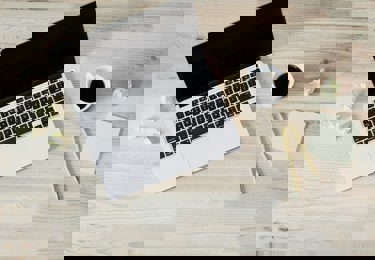 Dator på ett skrivbord med en kopp kaffe samt några pennor och papper.